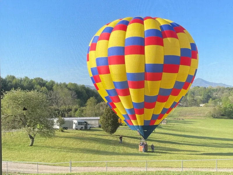A red, yellow and blue hot air balloon settling into a green field in Candler, basket just above the grass