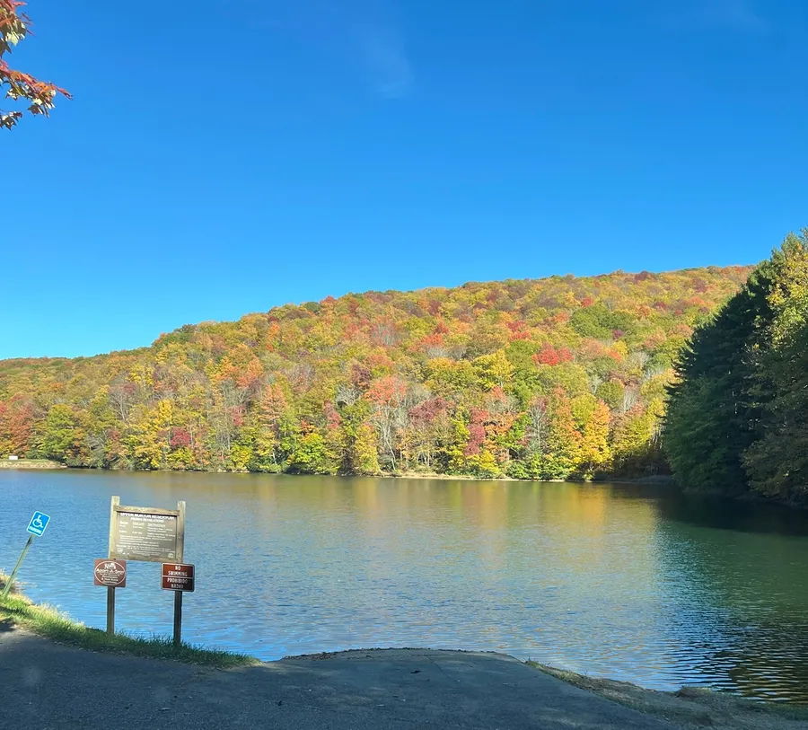 A still mountain reservoir reflecting a hillside of orange and yellow trees